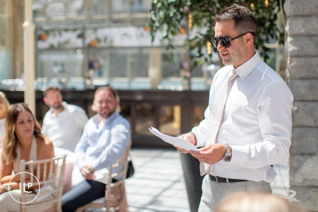 A best man wearing sunglasses reads his speech from notes during a luxury Gloucestershire wedding breakfast.