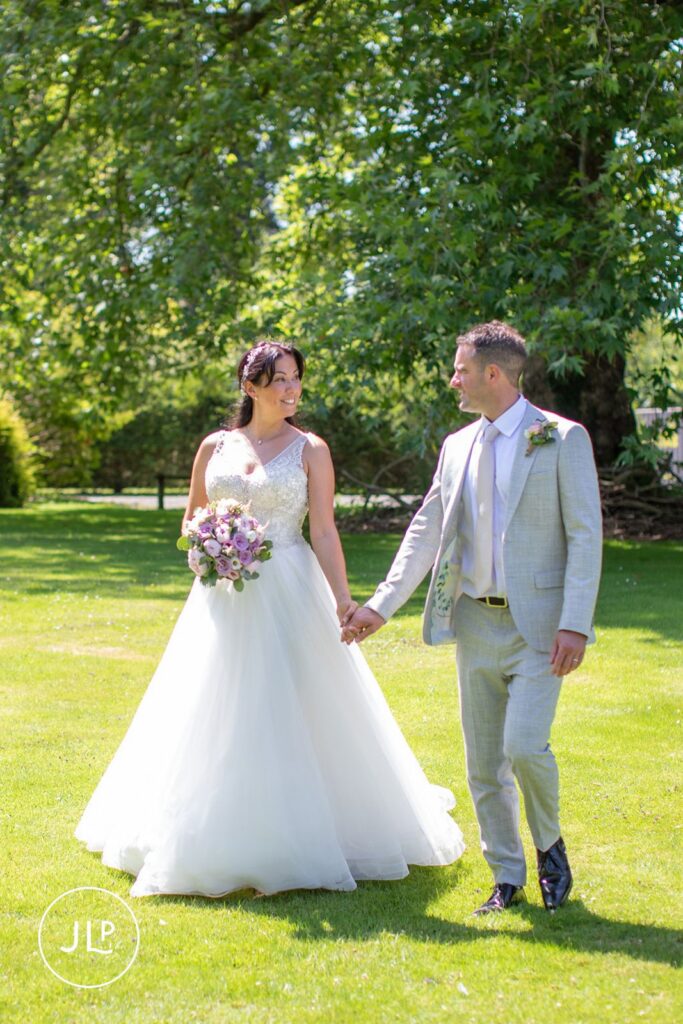 De Vere Tortworth Court wedding photography showing the couple walking hand-in-hand through the sun-drenched gardens.