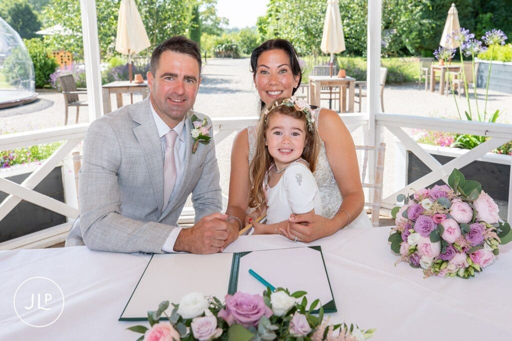 Bride, groom, and daughter signing marriage register at Tortworth Court wedding photographer shoot.