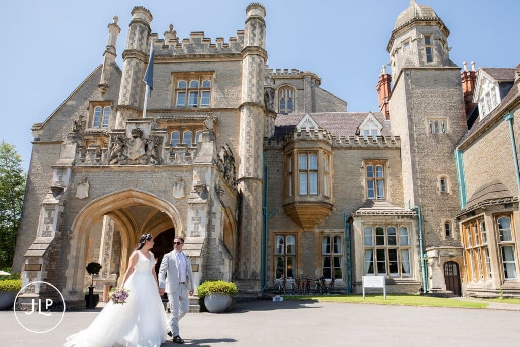 Bride and groom walking past the historic facade during a Tortworth Court wedding photographer session.