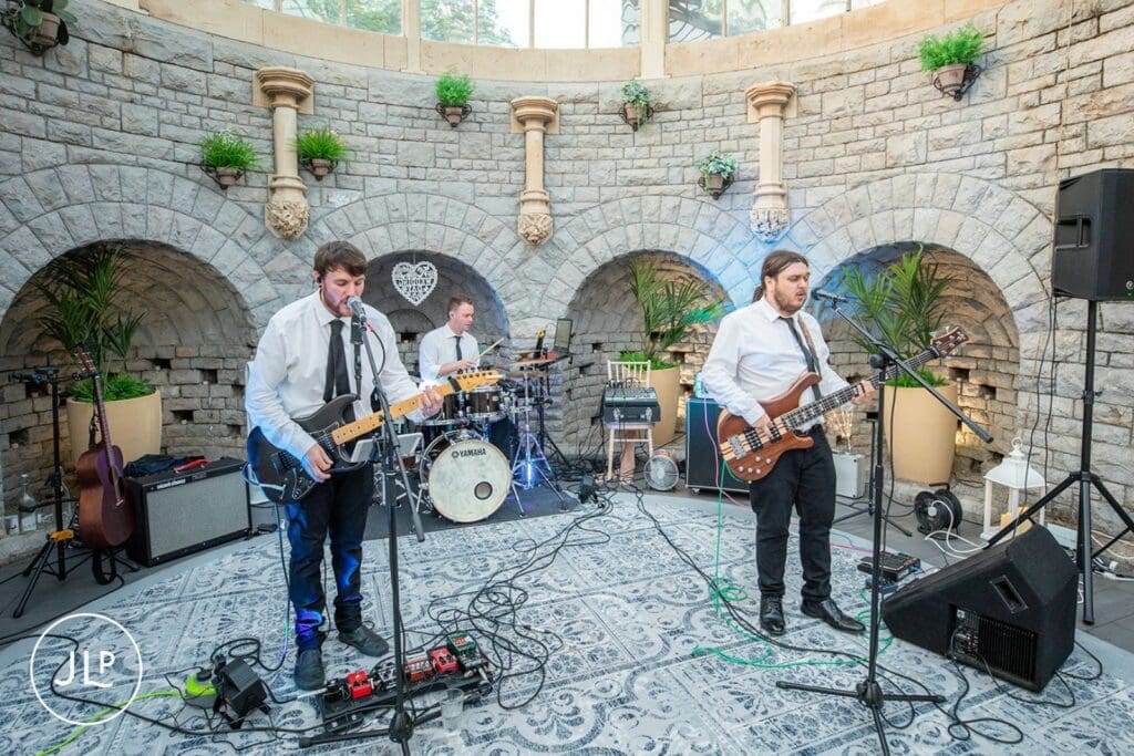 Live wedding band performing on stage under stone arches at a historic Gloucestershire wedding venue.