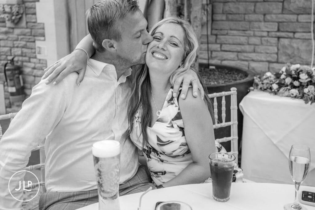 Man kissing a smiling woman on the cheek, captured by a natural wedding photography Gloucestershire professional.