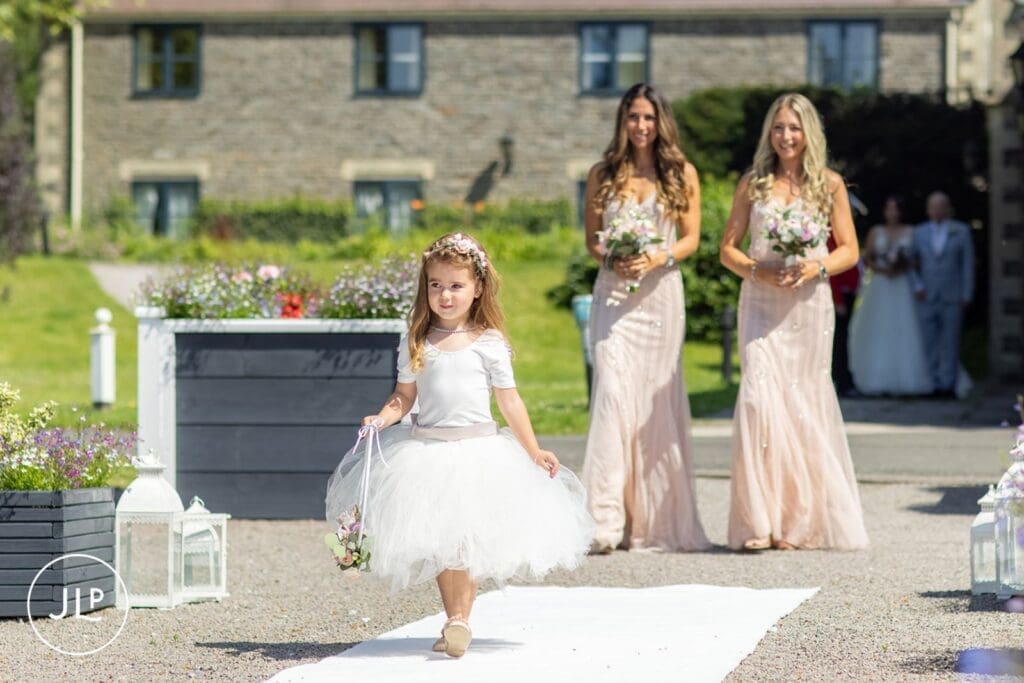 Adorable flower girl walking down the aisle at an outdoor wedding photographer UK ceremony.