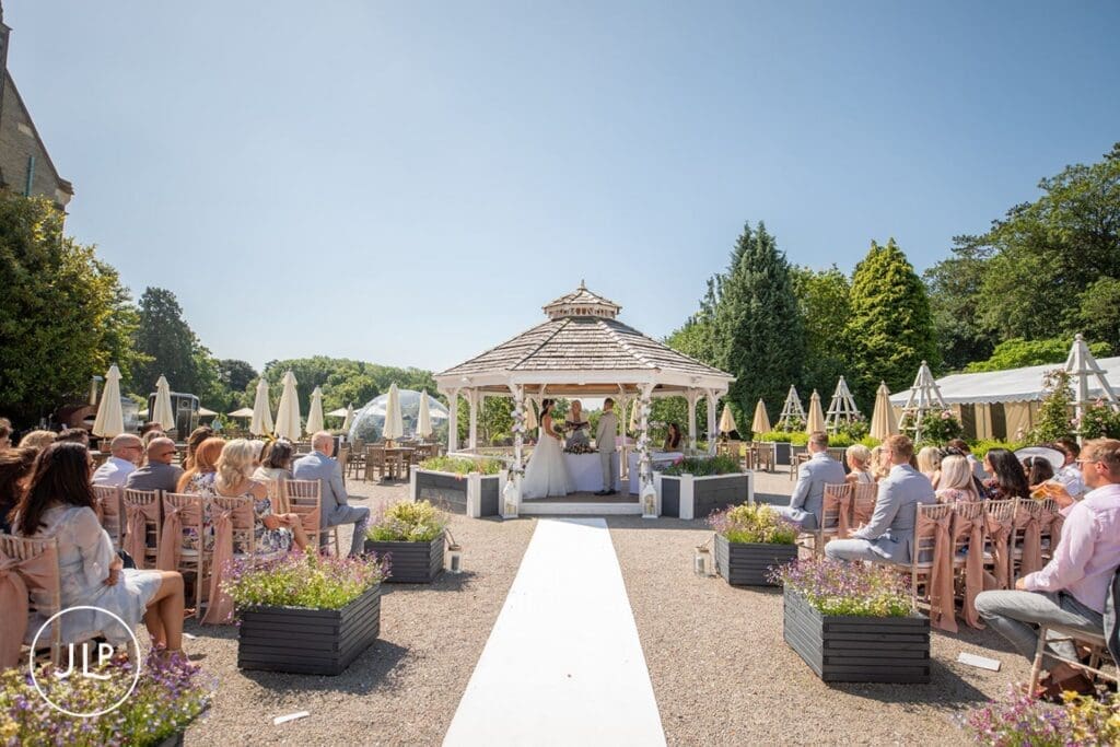 Wide shot of a beautiful garden gazebo ceremony by Tortworth Court wedding photographer.