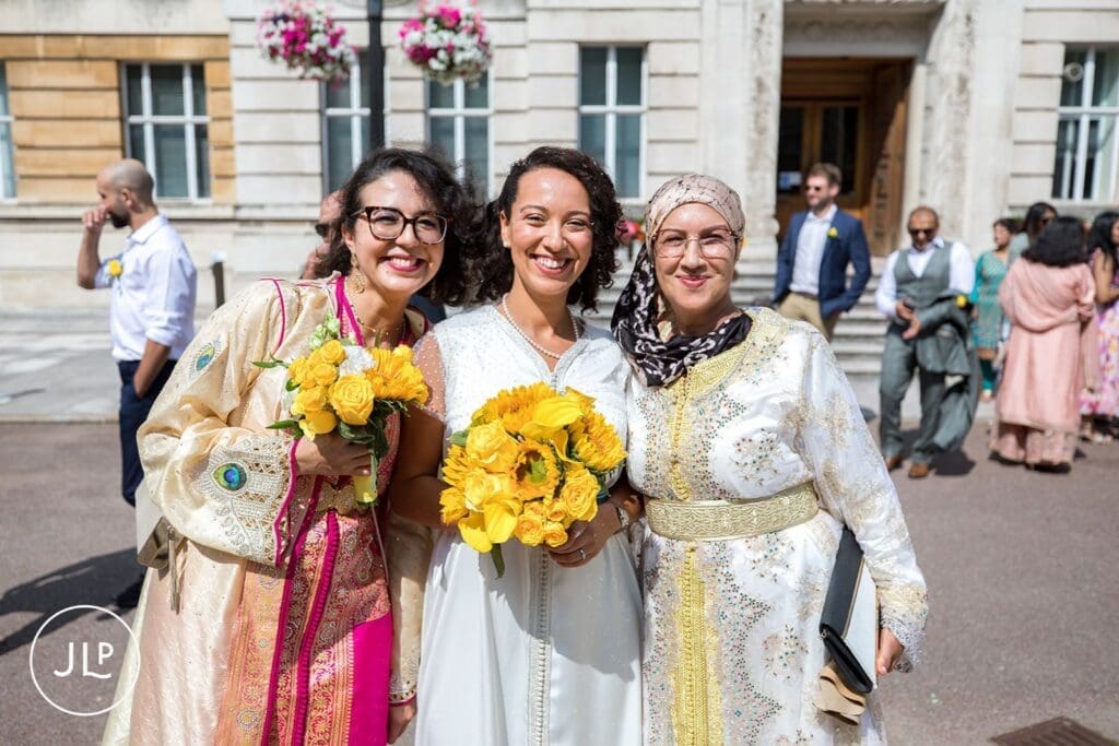 Smiling bride posing with wedding guests outside for South West London wedding photography.