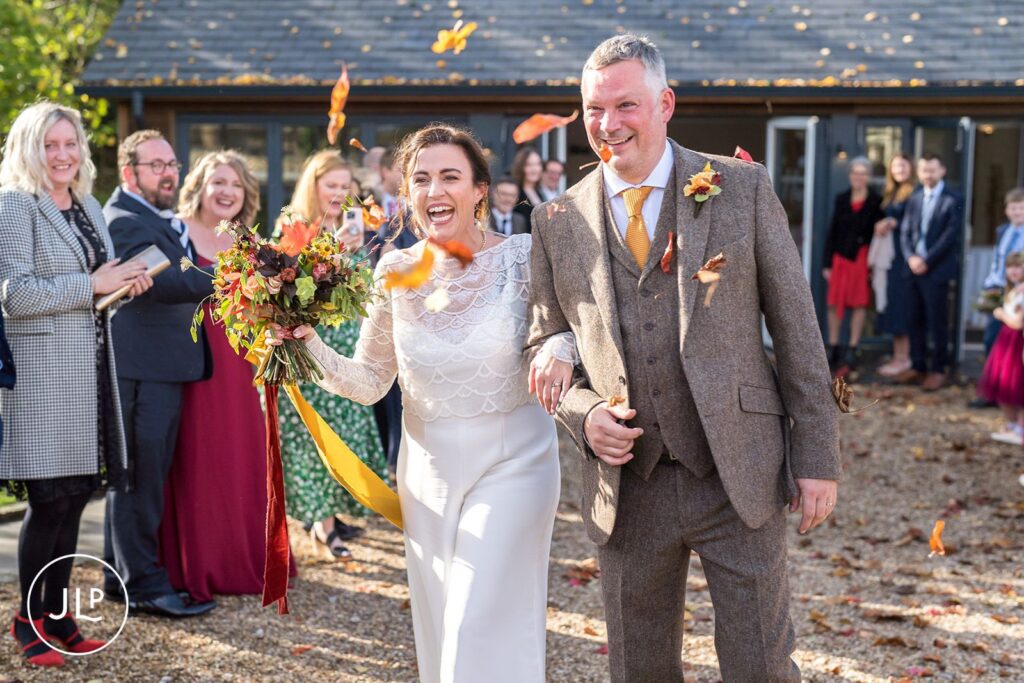 Fun wedding photography of a laughing bride and groom showered with autumn leaf confetti at Wasing Park.