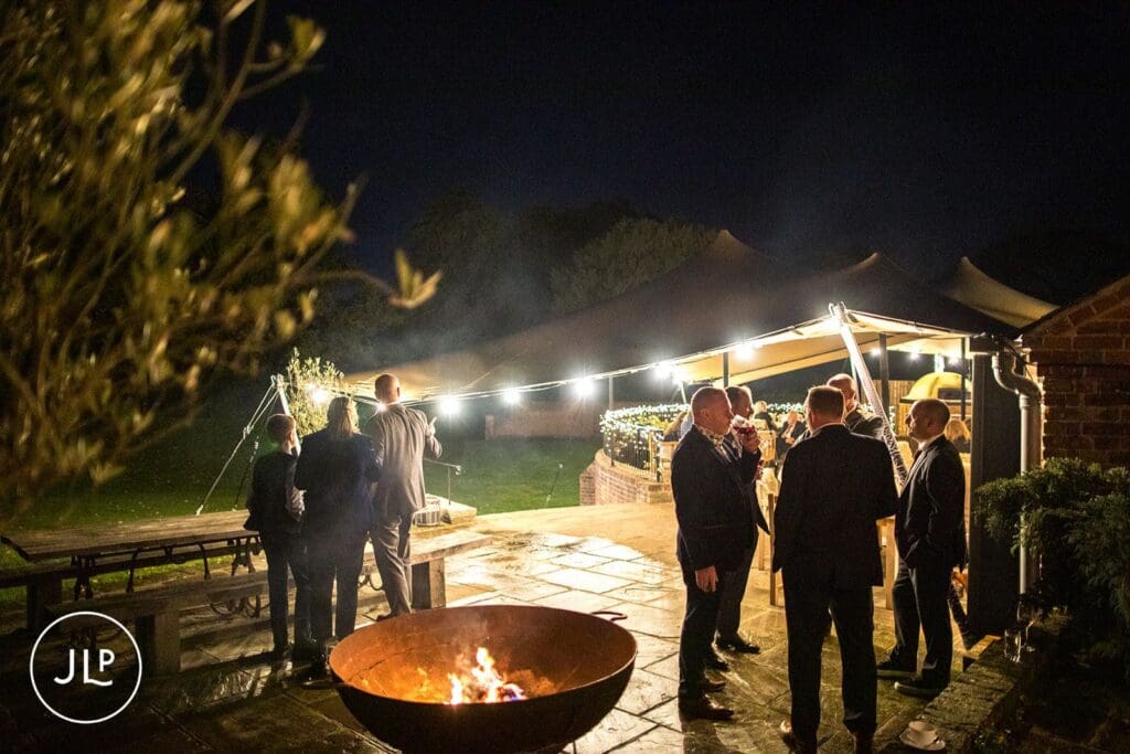 Guests mingling around an outdoor firepit at night during a luxury countryside wedding at Wasing Park Berkshire.