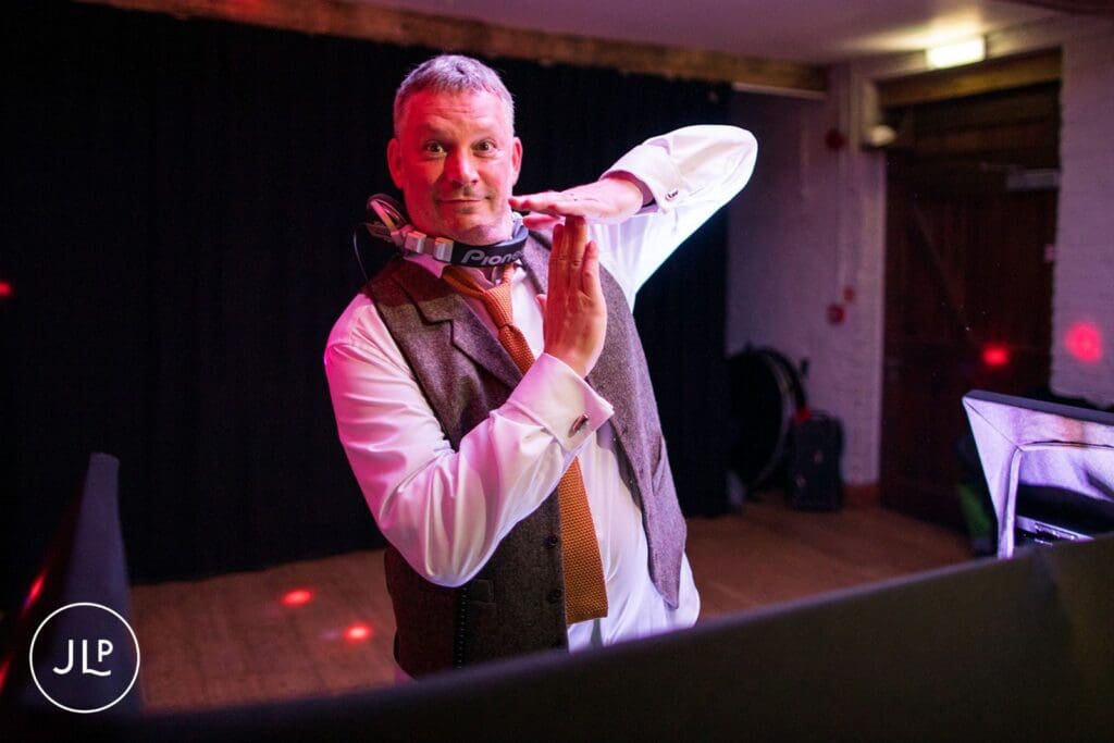 Groom wearing Pioneer headphones posing behind the DJ booth, captured by an autumn wedding photographer.