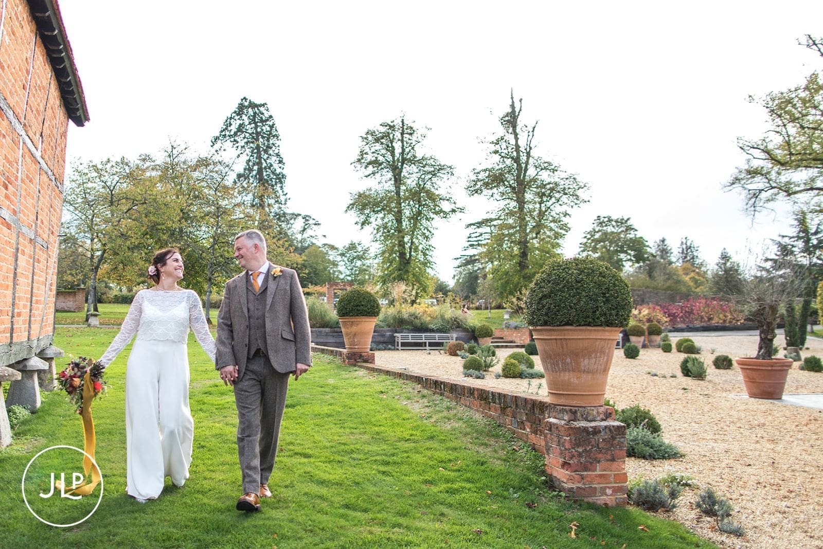 The bride and groom walking hand-in-hand past large terracotta planters on the lawn at Wasing Park.
