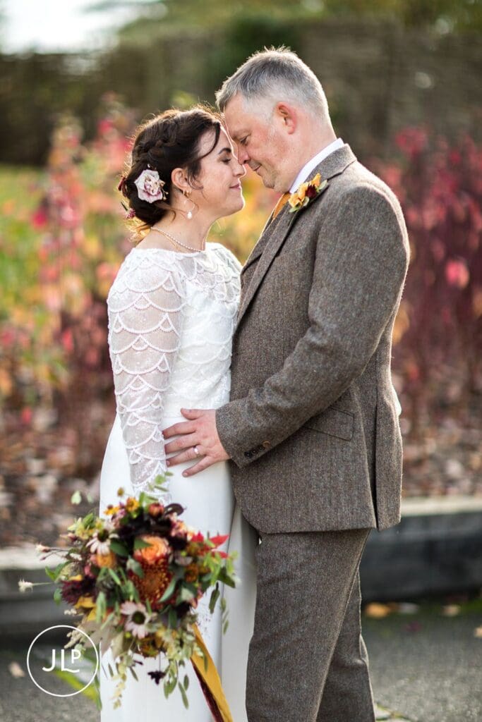 Romantic portrait by an autumn wedding photographer of a couple embracing amidst rich seasonal colours.