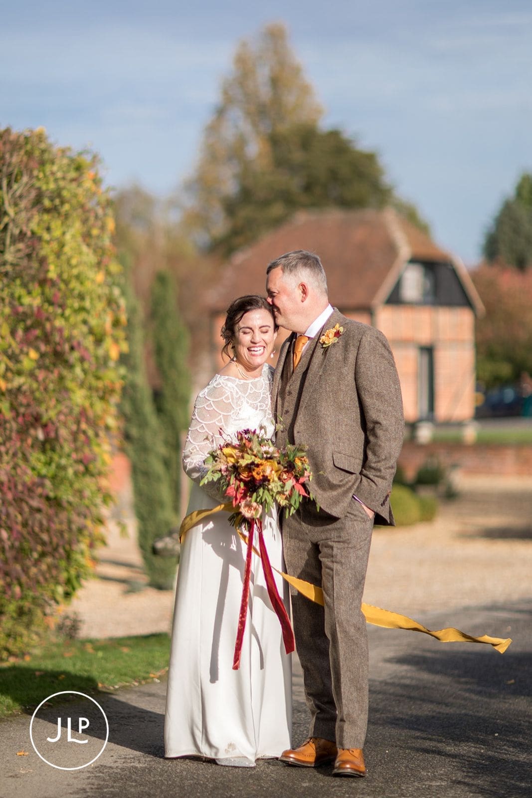 Happy newlyweds walking outside near rustic brick buildings during their autumn marriage celebration.