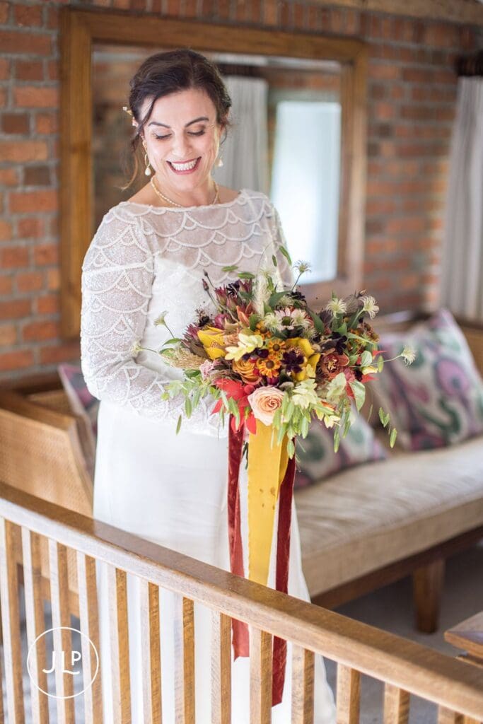 Natural wedding photography of a bride holding an autumn bouquet with burnt orange and red tones.