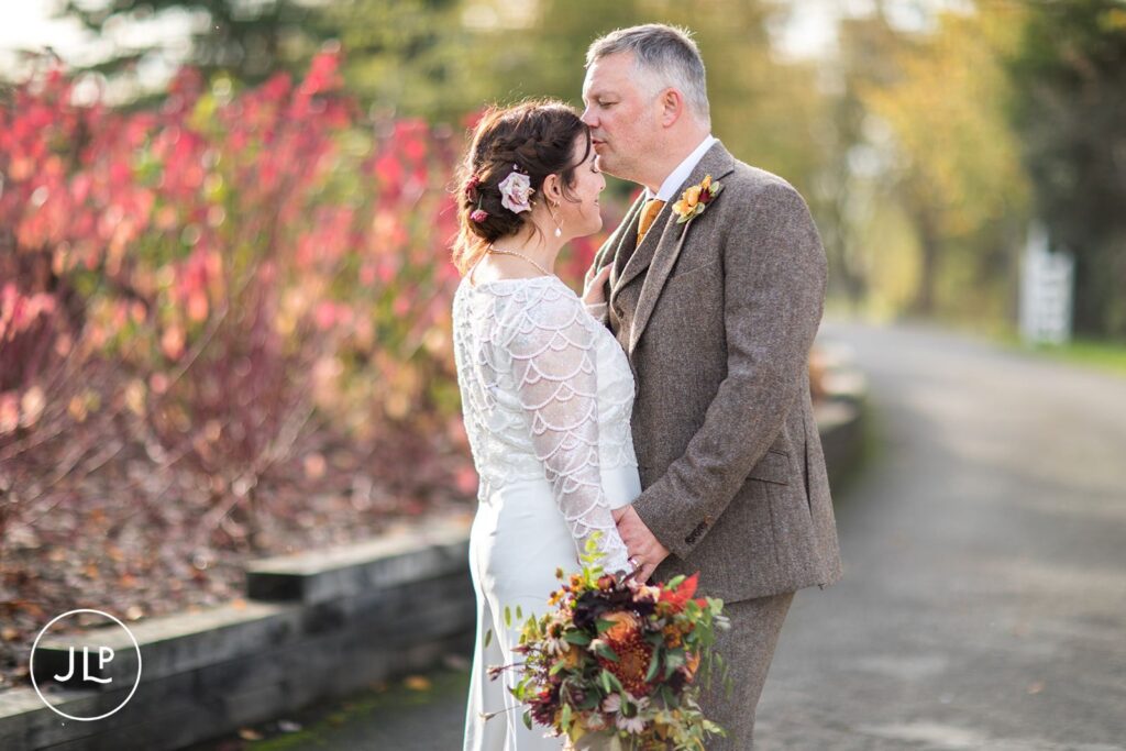 Wasing Park wedding photographer captures a tender forehead kiss against vibrant red autumn foliage.