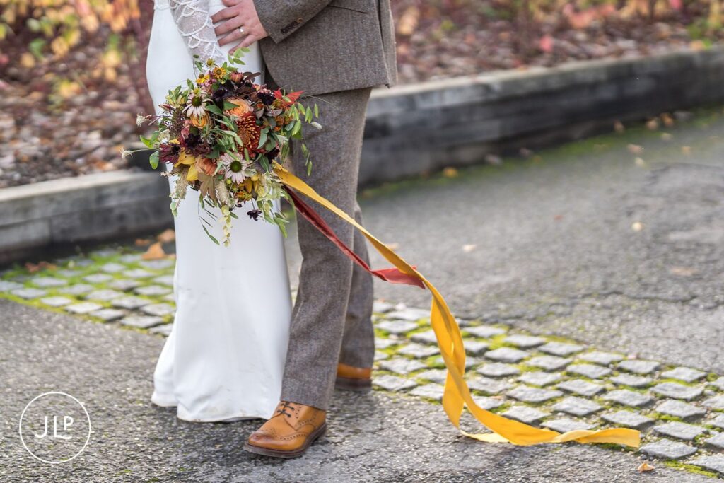 Autumn wedding inspiration showing a textured floral bouquet with long yellow silk ribbons on the path.