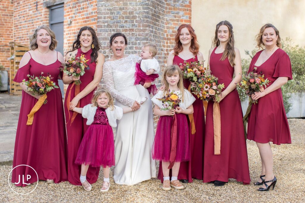 Fun wedding photography of a bride, flower girls, and bridesmaids in deep red dresses at a Wasing Park wedding.