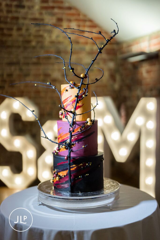 A three-tiered modern autumn wedding cake with burnt orange tones and black branches at Wasing Park.