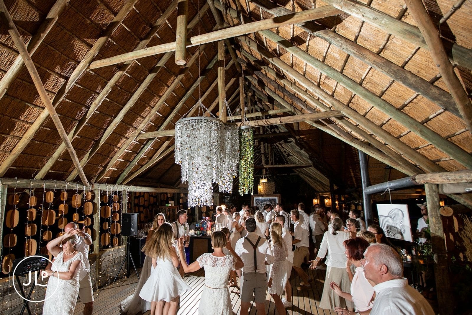 Wedding guests dancing under chandeliers inside a thatched luxury safari lodge in Botswana.