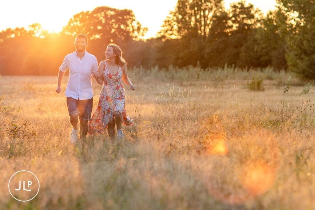 Excited couple running through a grassy field for a dynamic pre wedding photoshoot in the evening light.