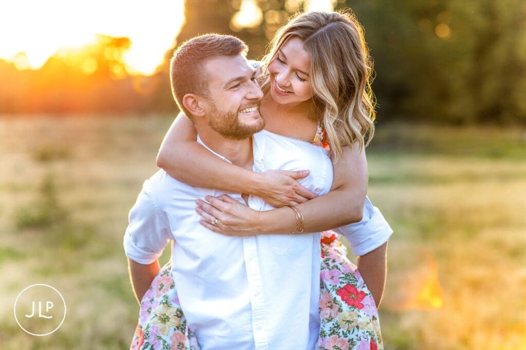 Man giving a piggyback ride to his fiancée during a natural engagement photography session at sunset.