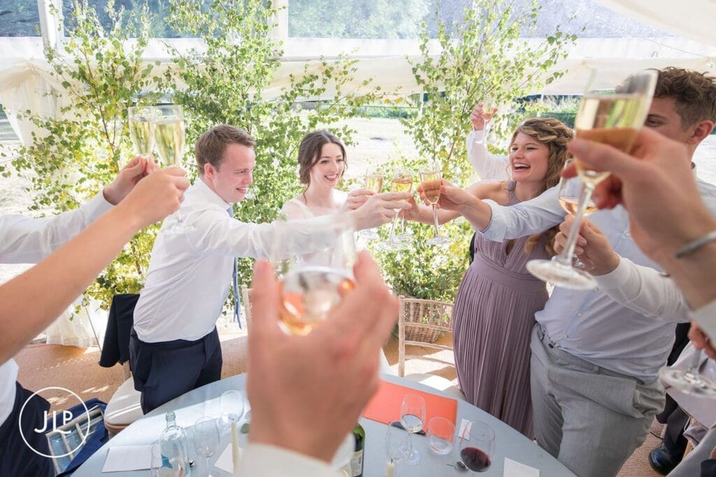 Bride, groom, and wedding guests raising a champagne toast inside a luxury marquee wedding setup.