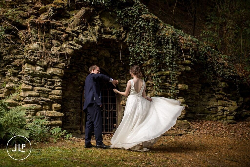 A groom twirling his bride during a beautiful lakeside wedding in Surrey near an old stone structure.