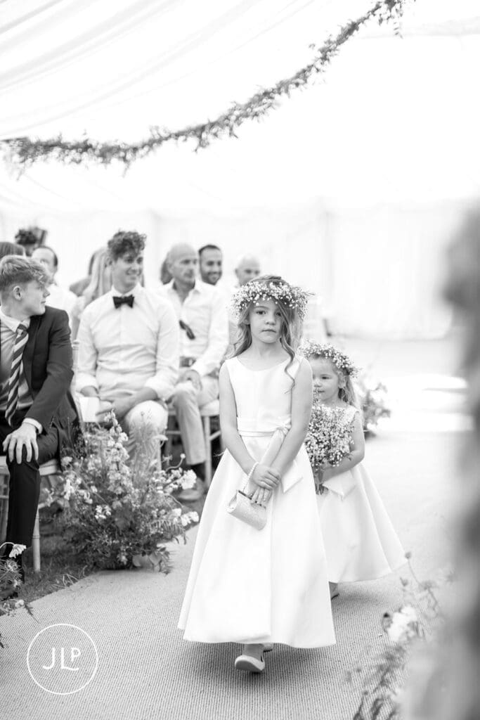 A young flower girl in a white dress walking down the aisle, capturing genuine marquee wedding inspiration.