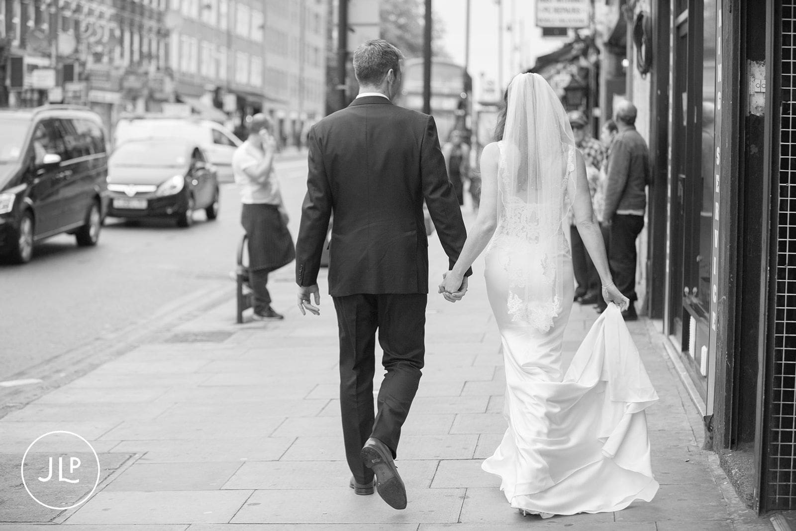 A stylish bride and groom holding hands while crossing a street in North London.