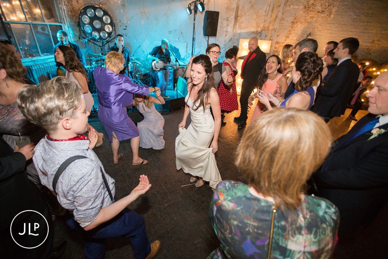 Bride dancing on the crowded dance floor with guests during her lively warehouse wedding reception.