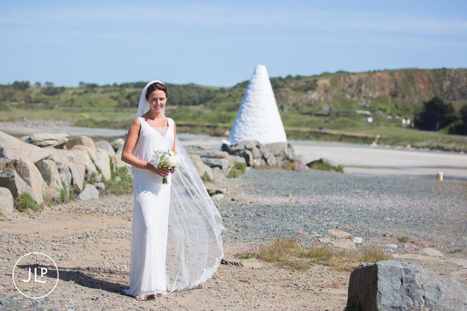 Bride standing on a rocky coastal path with a white beacon background, beautiful Alderney wedding photography.