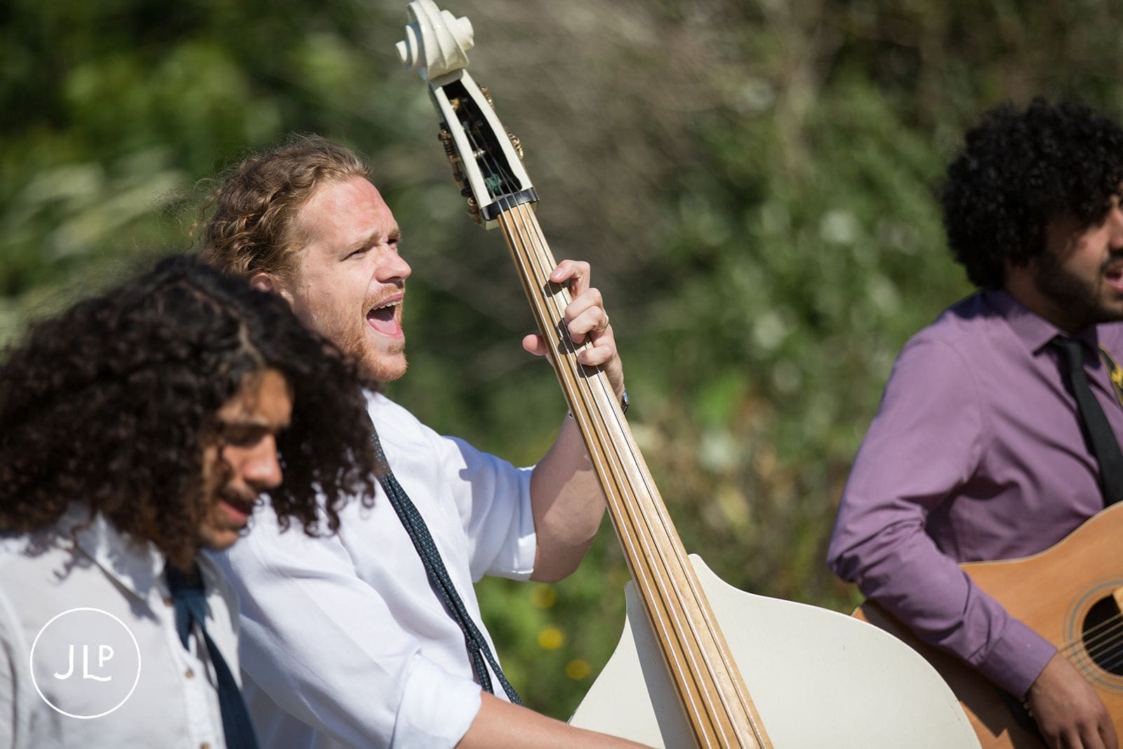 Wedding band musicians singing and playing a double bass and guitar outdoors for an Alderney celebration.