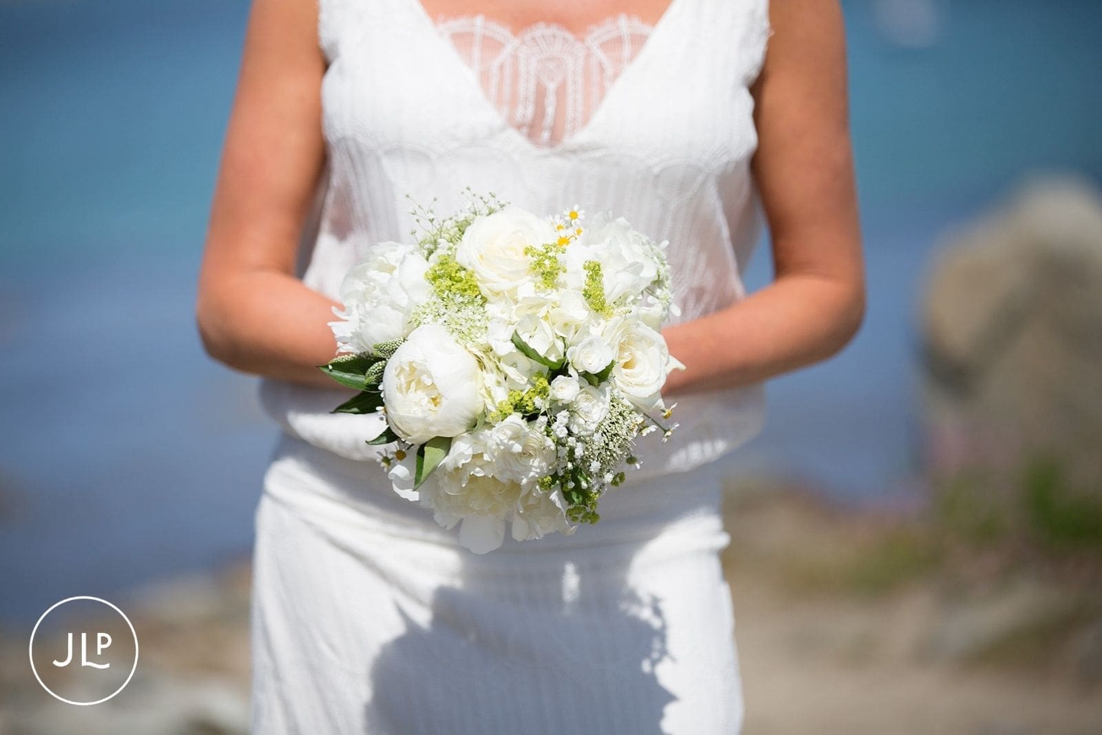 Close-up of a bride holding a delicate bouquet of white peonies and roses for an island marriage ceremony.