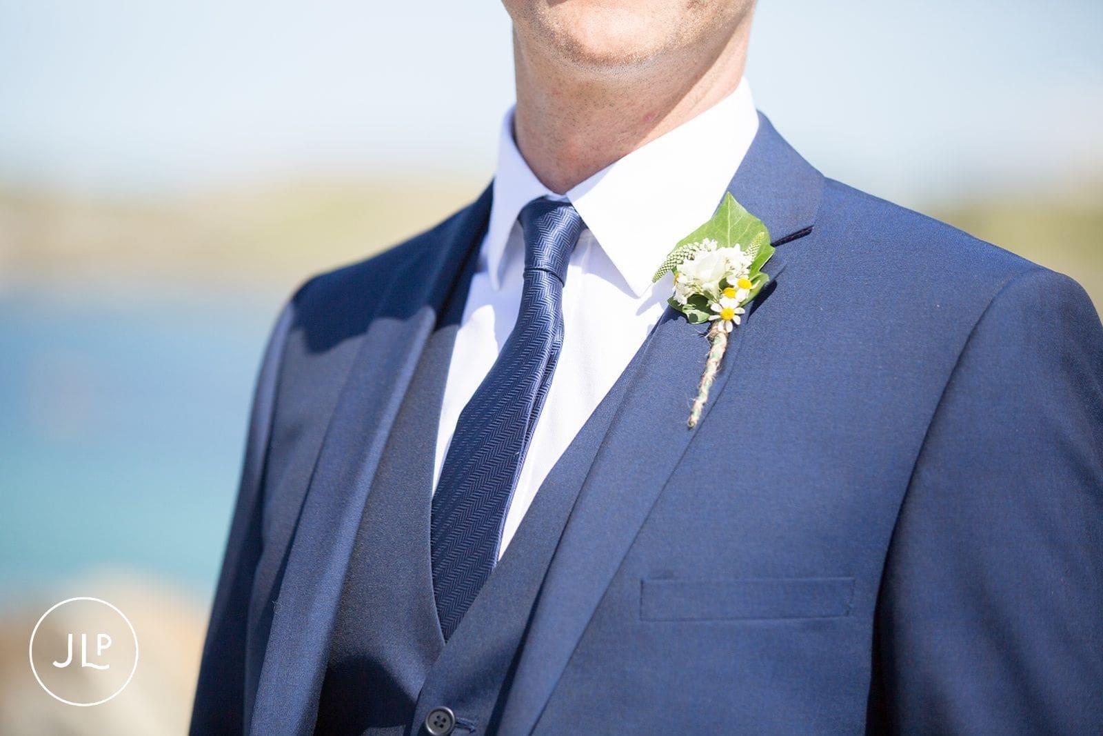 Close-up of a groom's blue suit, tie, and delicate white wildflower buttonhole for an island nuptial.