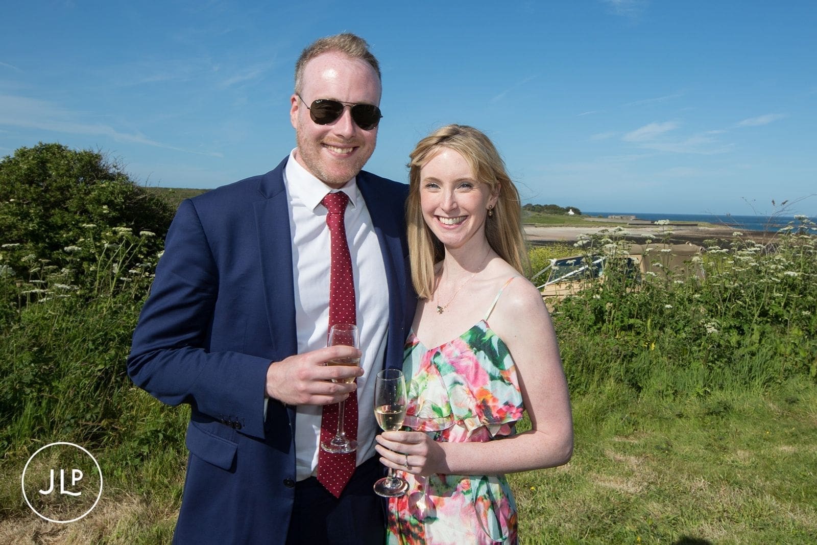 Smiling guests holding champagne glasses outside at a scenic island destination wedding.