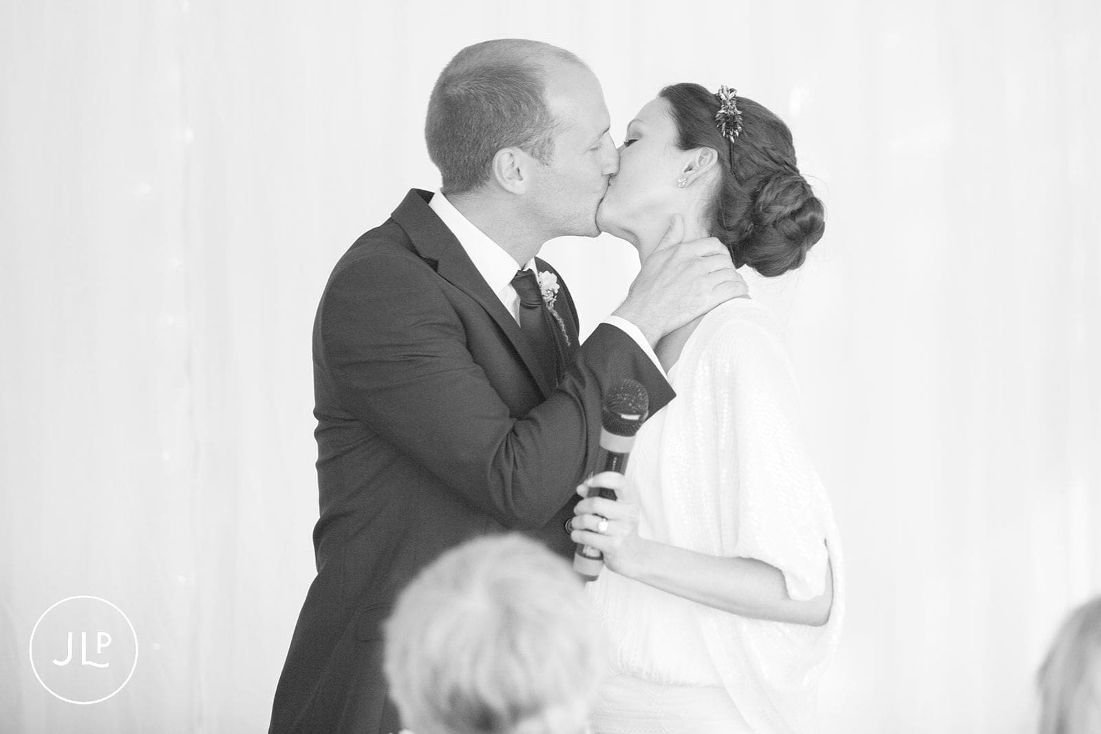 Black and white close up of a bride and groom sharing a romantic kiss during wedding speeches.