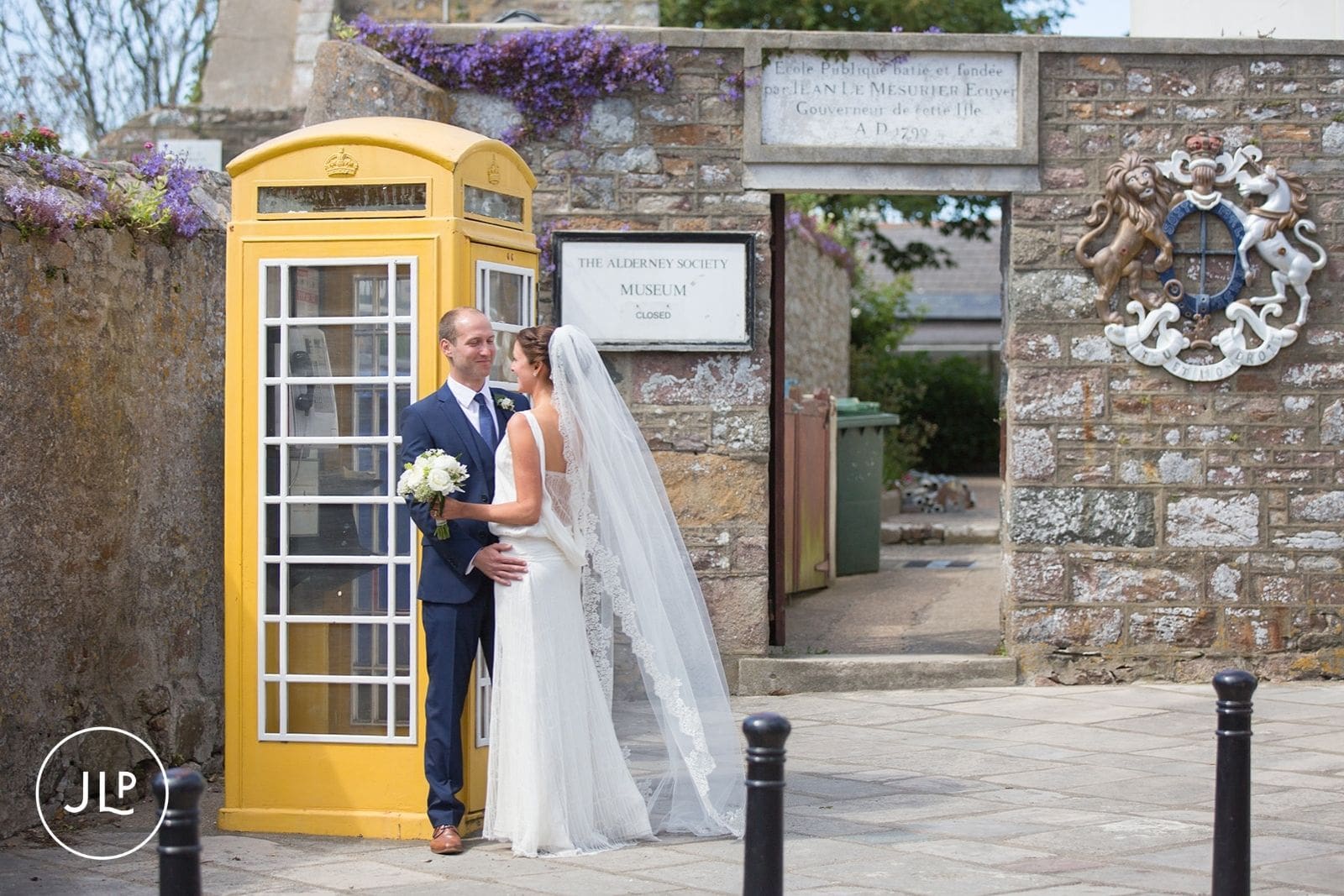 Bride and groom posing by the iconic yellow phone box outside the museum, Alderney wedding photography.