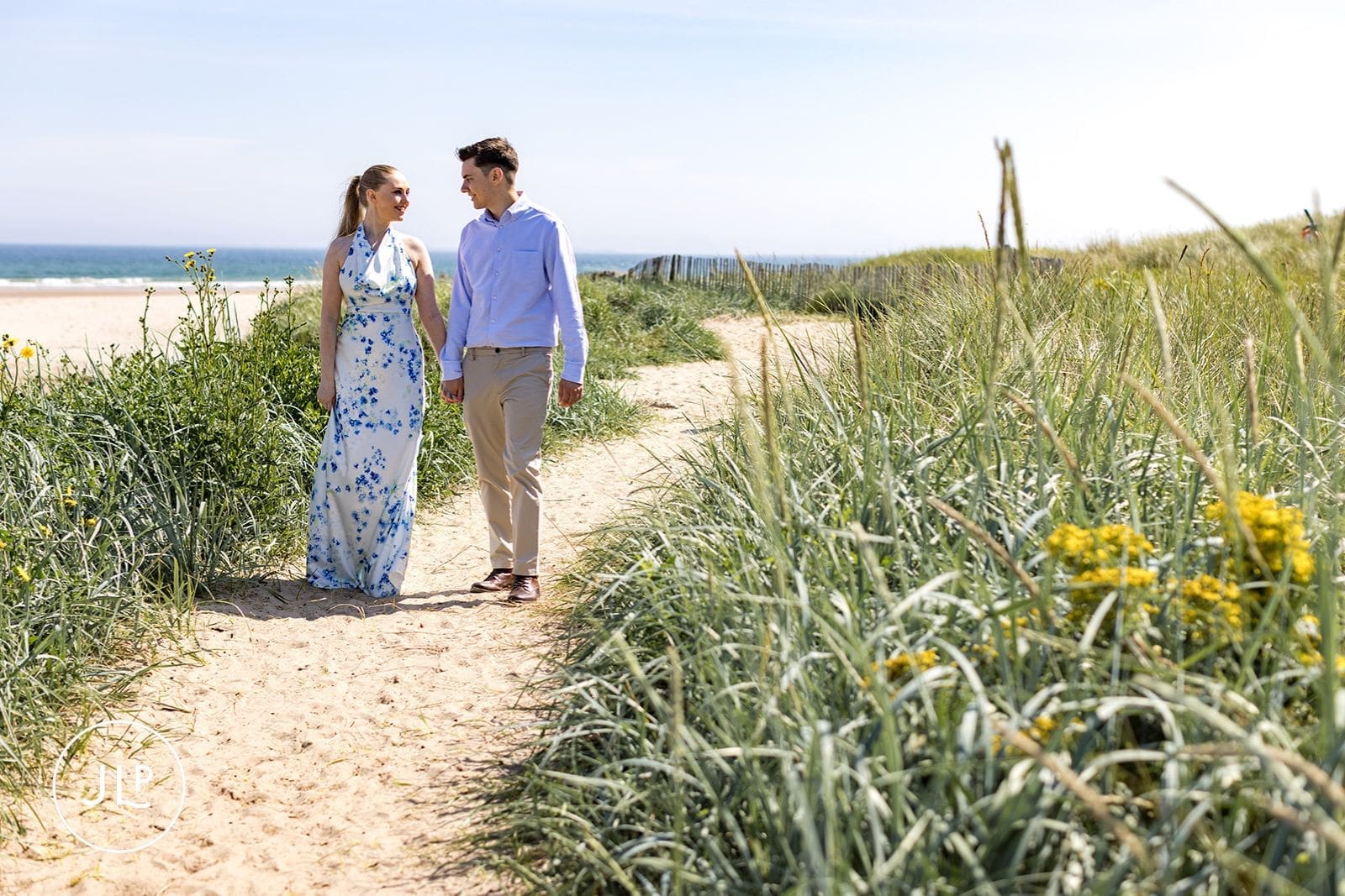 Candid beach engagement photography of a couple strolling along a sandy path.