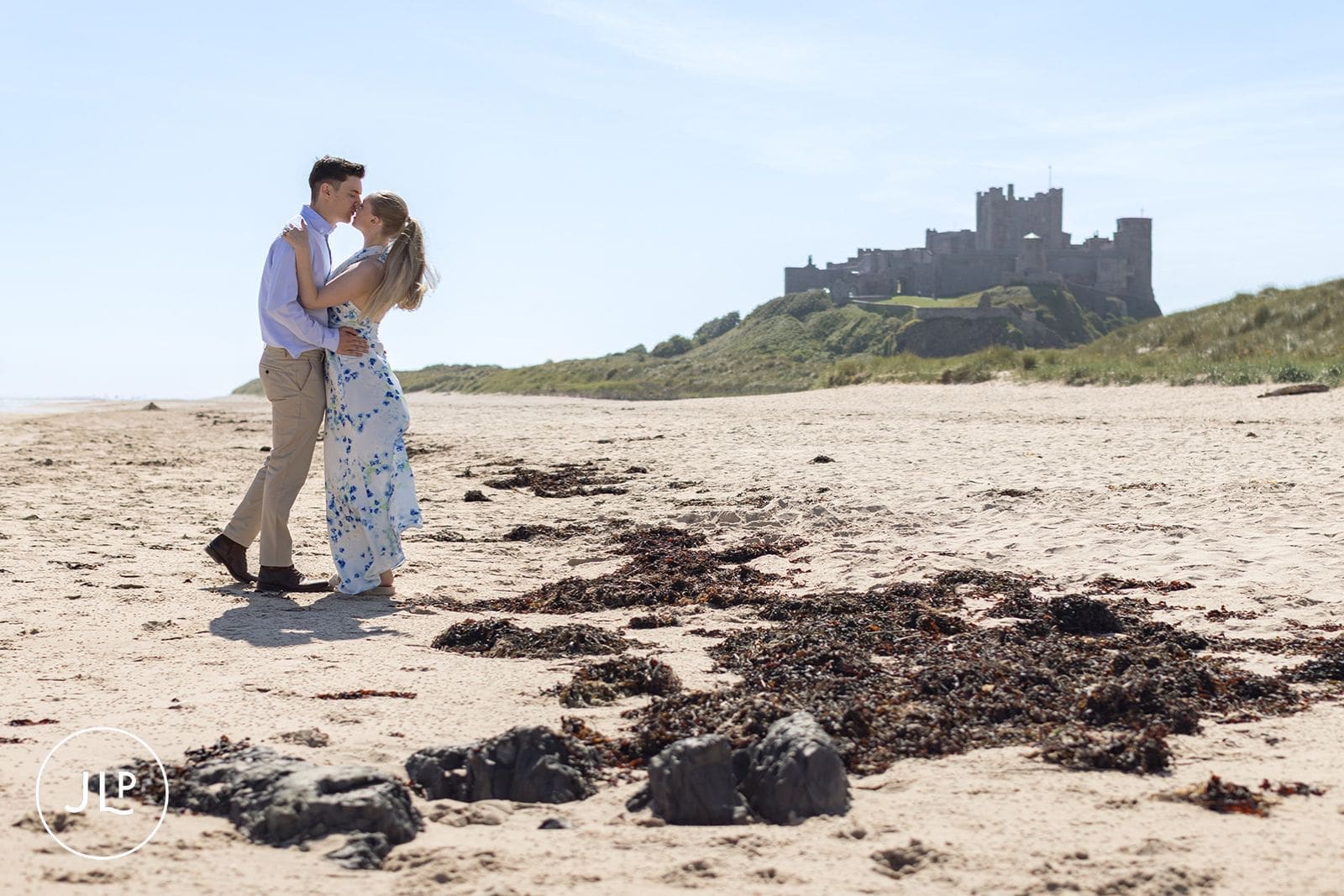 Romantic couple kissing on a sandy shore with the historic Bamburgh Castle backdrop.