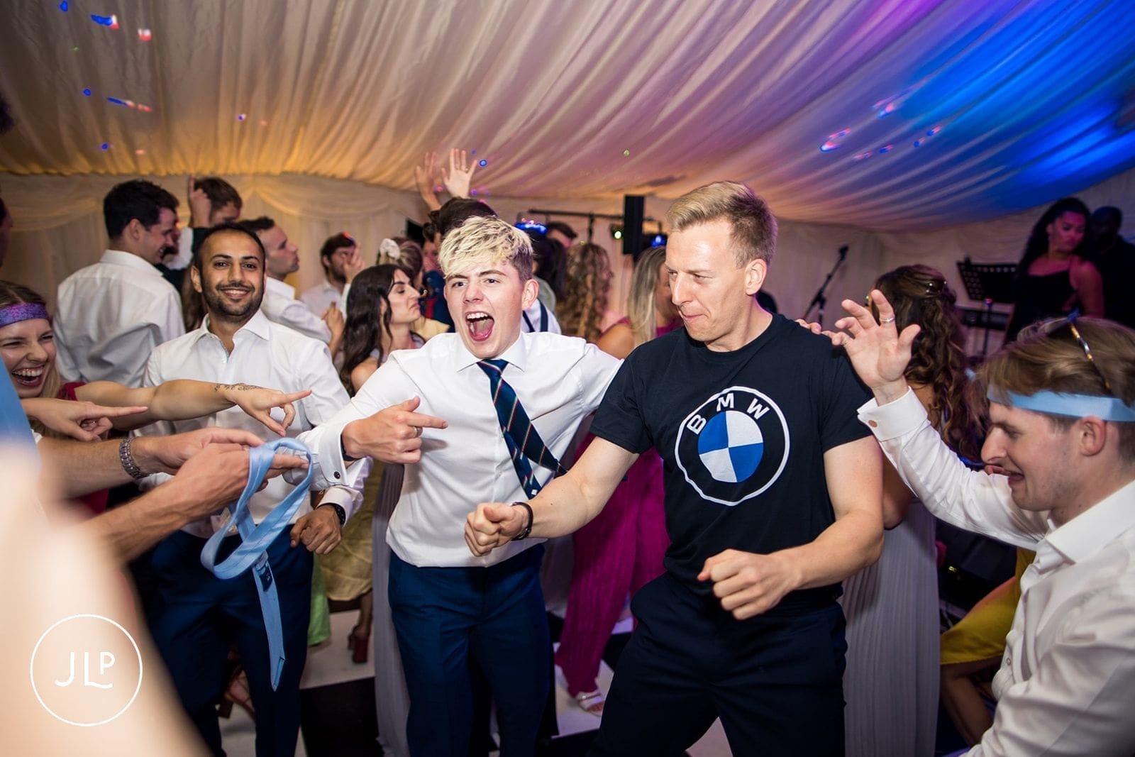 Energetic wedding guests singing and dancing on a packed dance floor during the evening reception party.