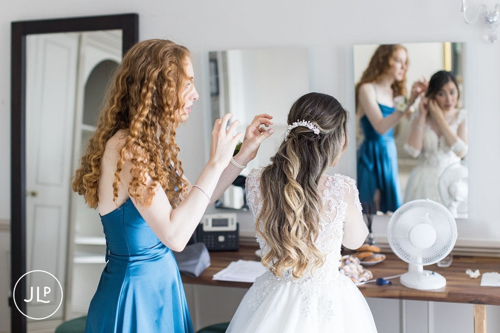 A bridesmaid helping the bride adjust her hair accessory in the bridal suite during morning preparation.