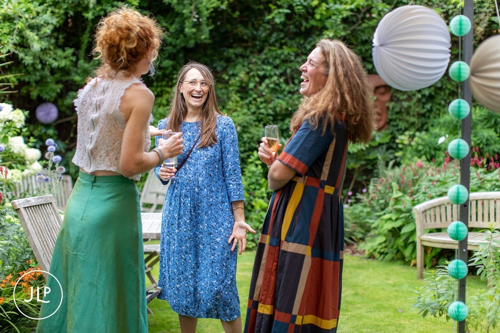 Guests laughing and drinking champagne during a relaxed garden wedding reception cocktail hour.