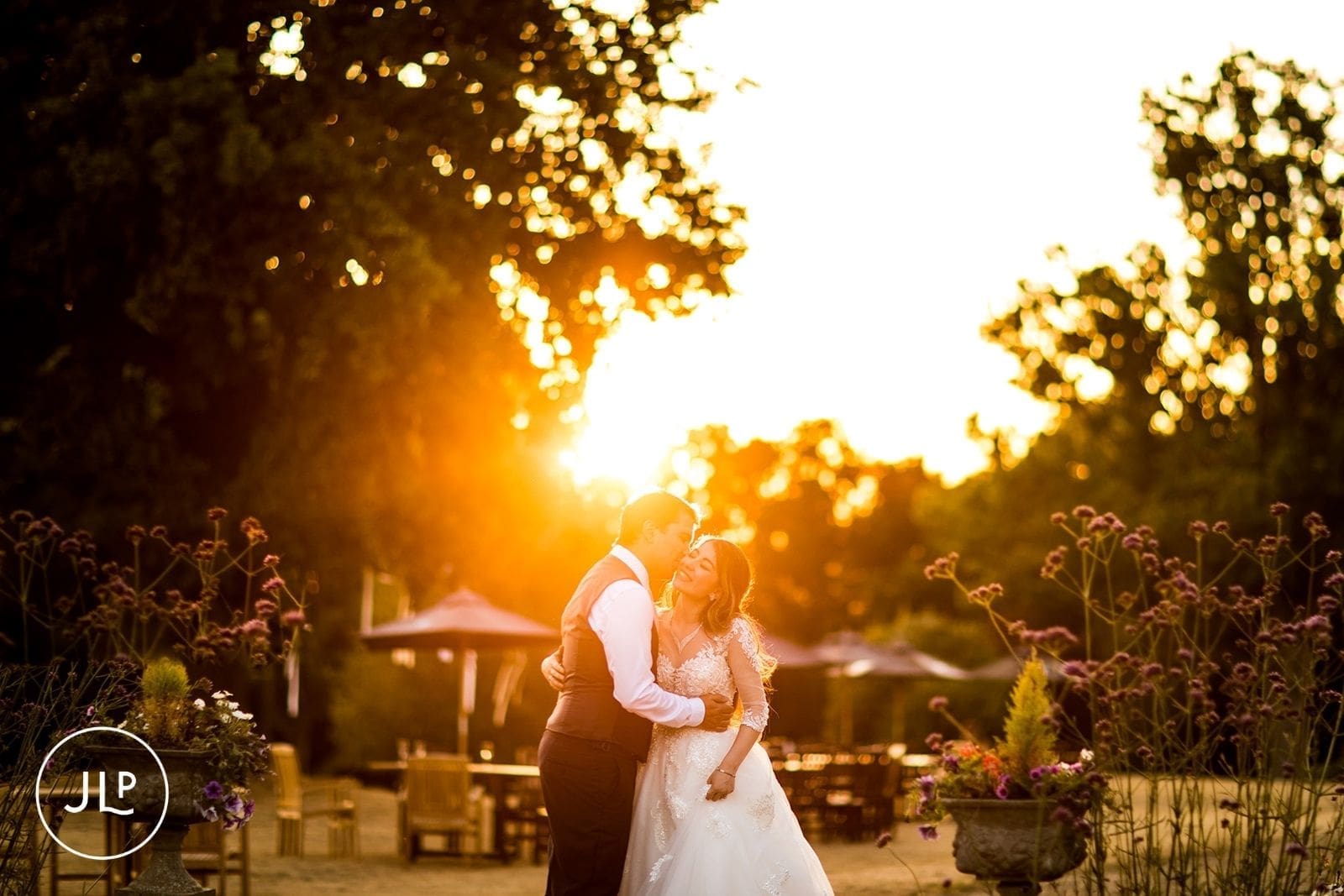 A romantic golden hour wedding couple portrait with warm, glowing sun flare in a beautiful garden setting.