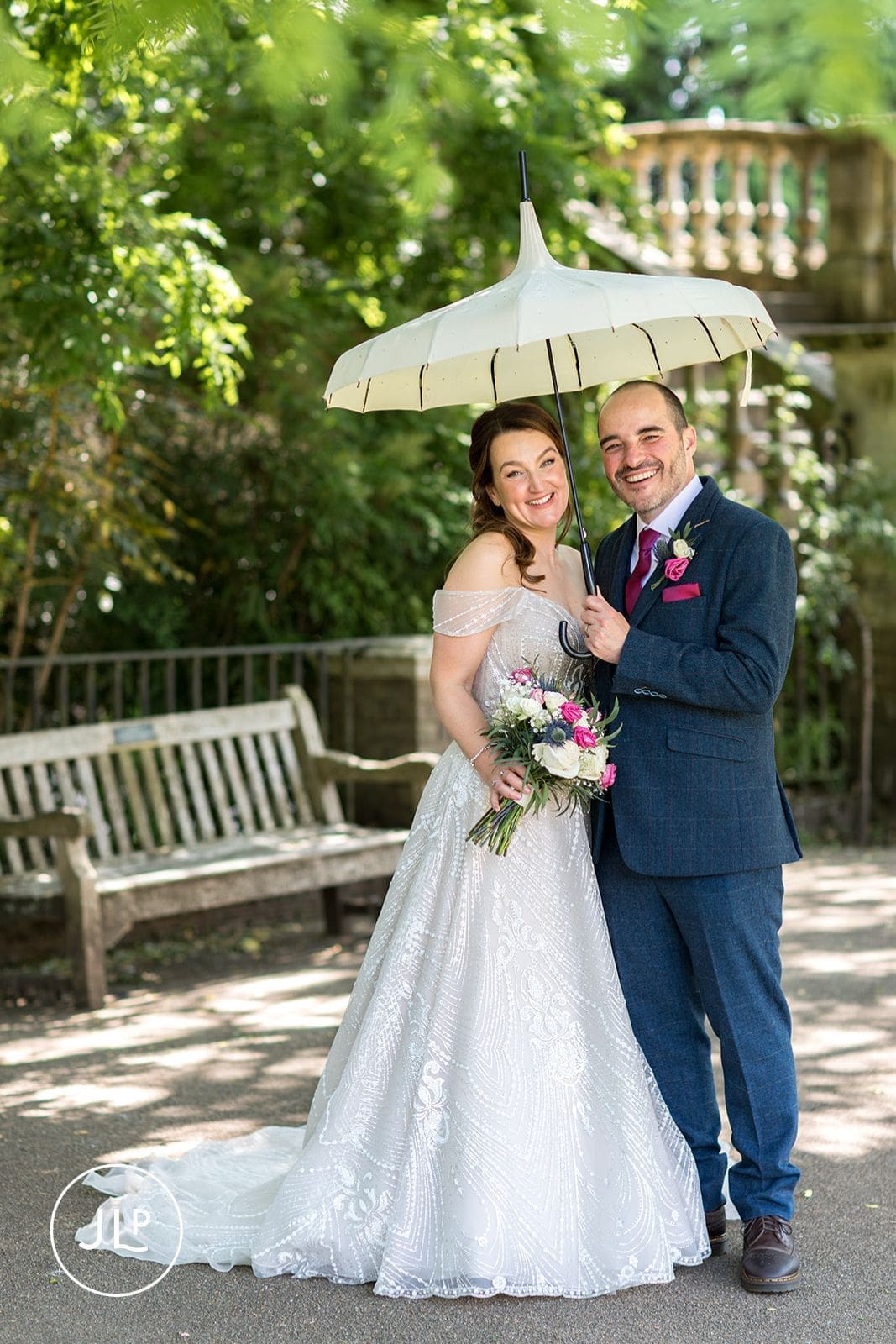 : Happy bride and groom smiling under a white umbrella, showing a plan B for rainy British wedding weather.